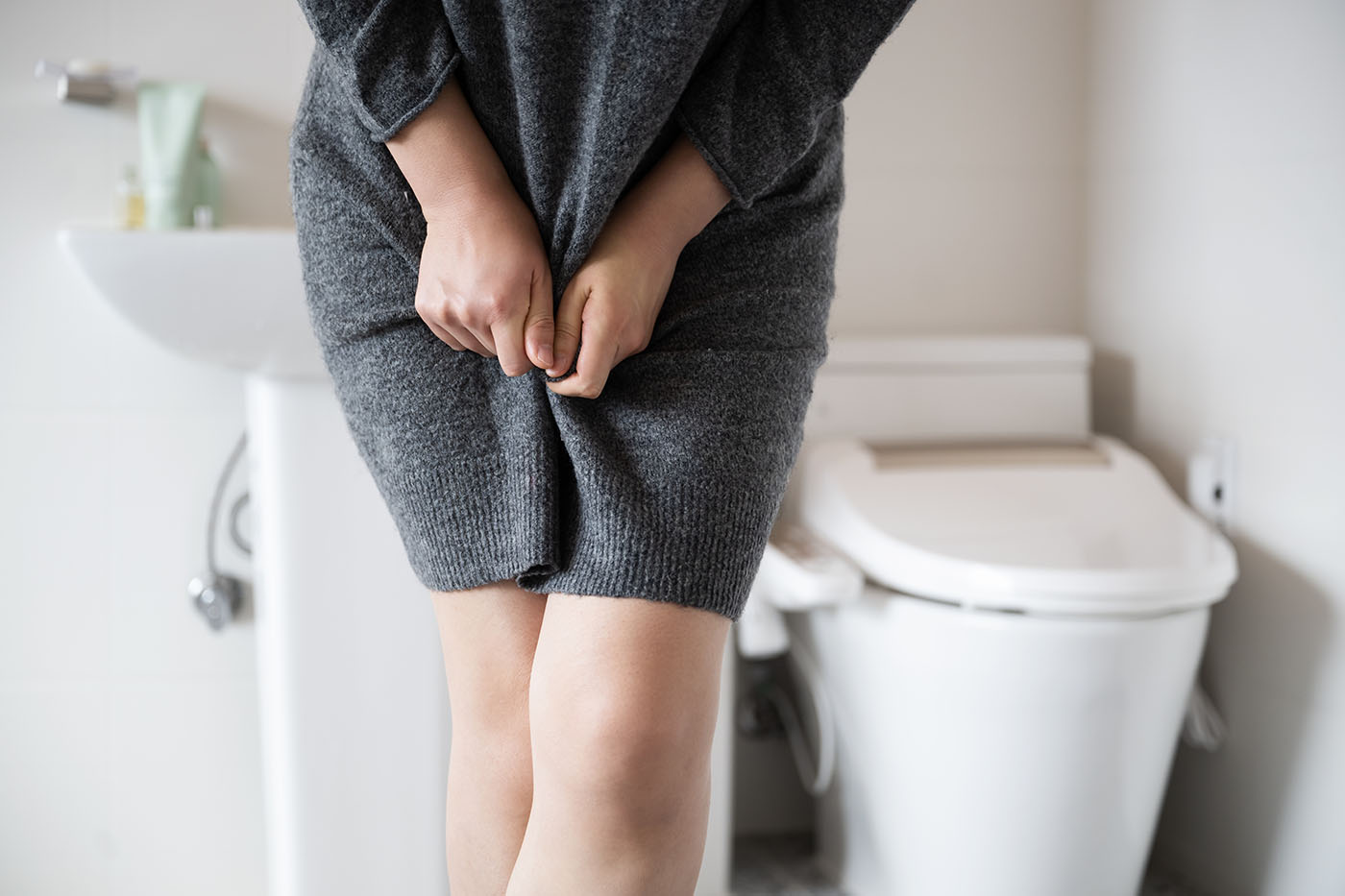 Harninkontinenz Frau, die vor einer Toilette steht und die Beine überkreuzt, weil sie dringend zur Toilette mussl