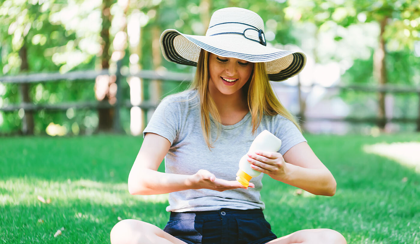 Frau mit Hut im Park, die sich mit Sonnencreme vor der Sonne schützt
