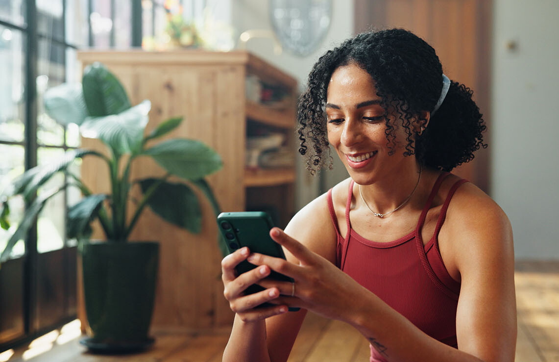 MASV-Kurs Lächelnde Frau mit Handy, die zu Hause die MINDZEIT App nutzt