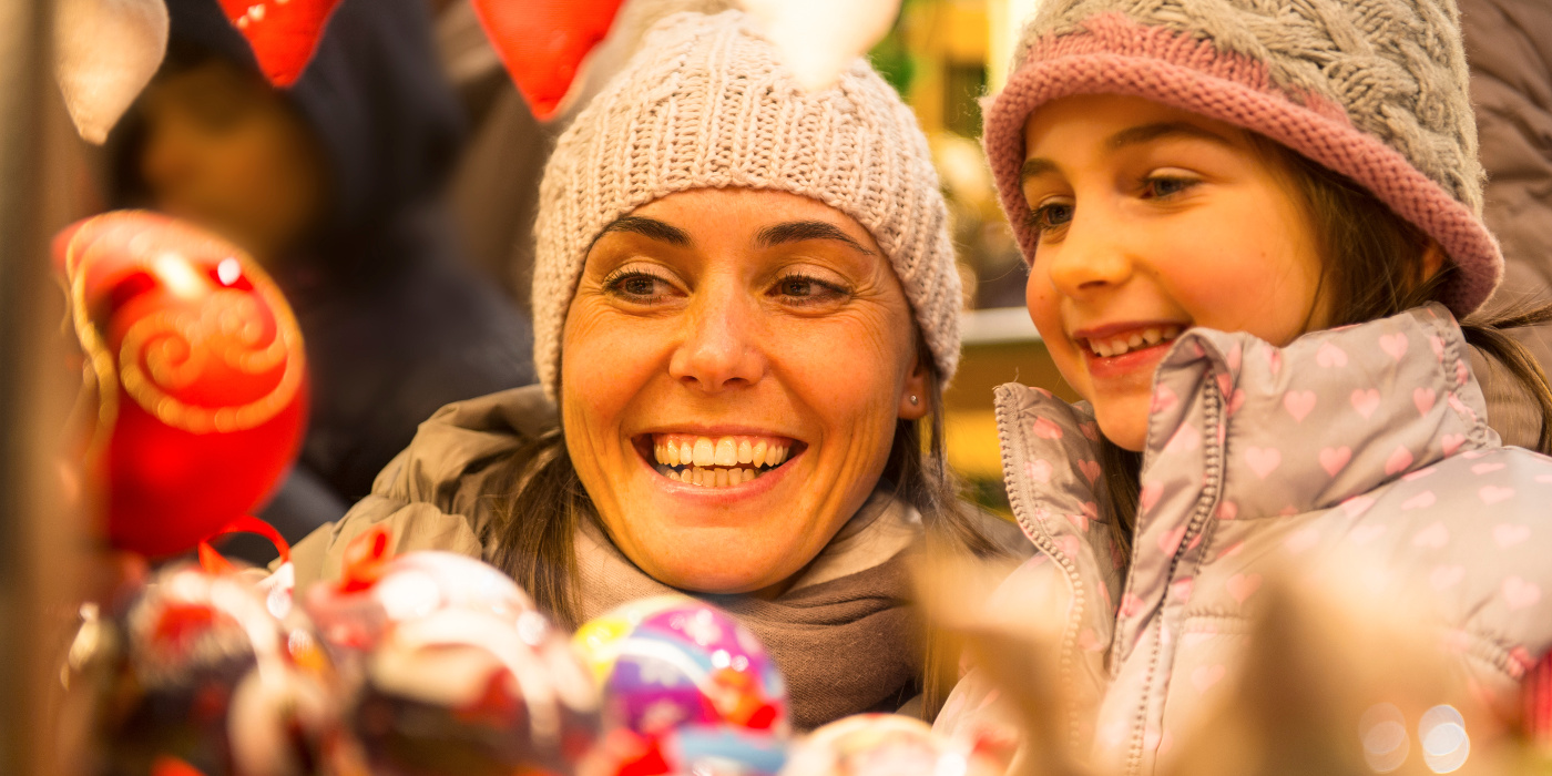 Mutter mit Tochter an einem Weihnachtsmarktstand mit Christbaumkugeln