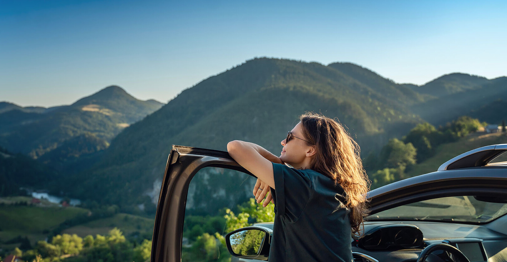 Frau steht an einer offenen Autotür und schaut auf die Berge