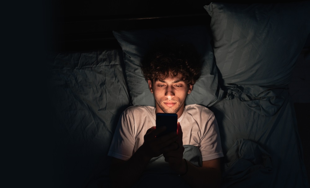 Junger Mann im Bett am Handy