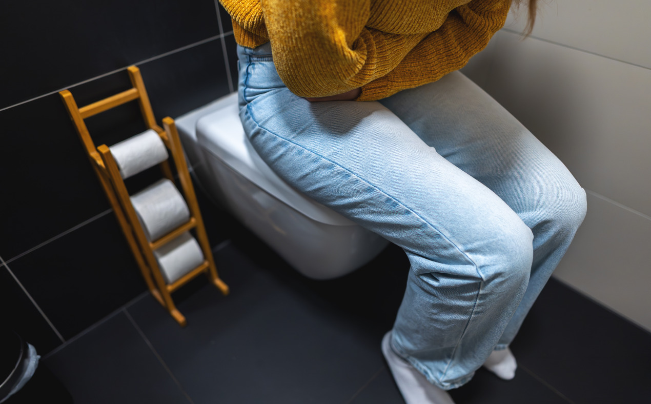 Bauchschmerzen Junge Frau sitzt mit Bauchschmerzen auf der Toilette