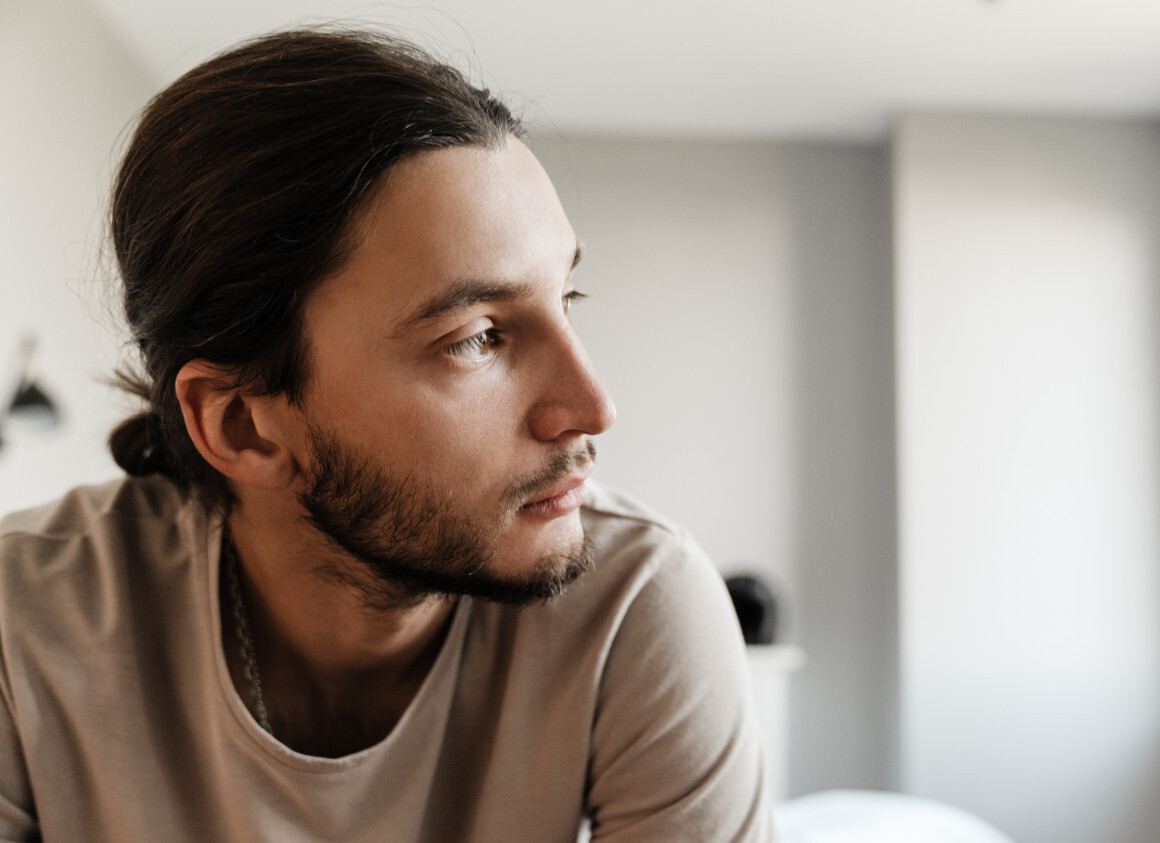 Junger Mann sitzt im Schlafzimmer und schaut traurig zur Seite