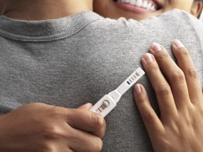 Glückliche junge Frau die positiven Schwangerschaftstest in der Hand hält und ihren Freund umarmt.