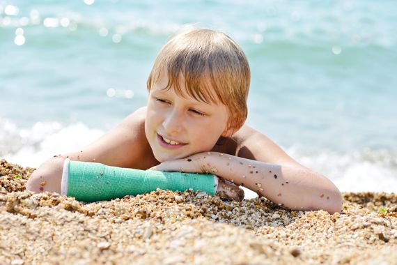 Eine Junge mit eingegipstem Unterarm liegt am Strand und macht einen glücklichen Eindruck.