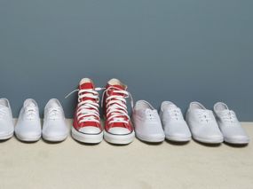 Weiße Schuhe, aufgereiht vor einer Wand, mit einem auffälligen Paar roter Schuhe im rechten Drittel des Bildes.