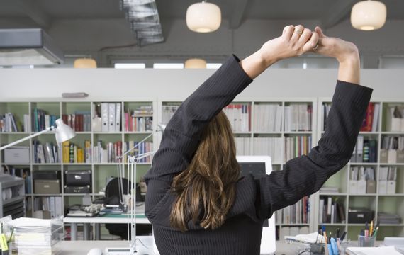 Frau macht Stretchingübungen am Büroschreibtisch