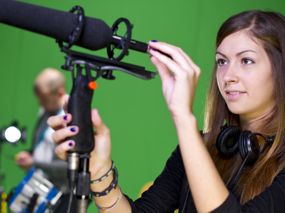 Junge Frau mit Mikrophon vor einem Greenscreen.