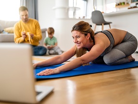 Frau, die Online-Fitness macht, mit ihrer Familie im Hintergrund